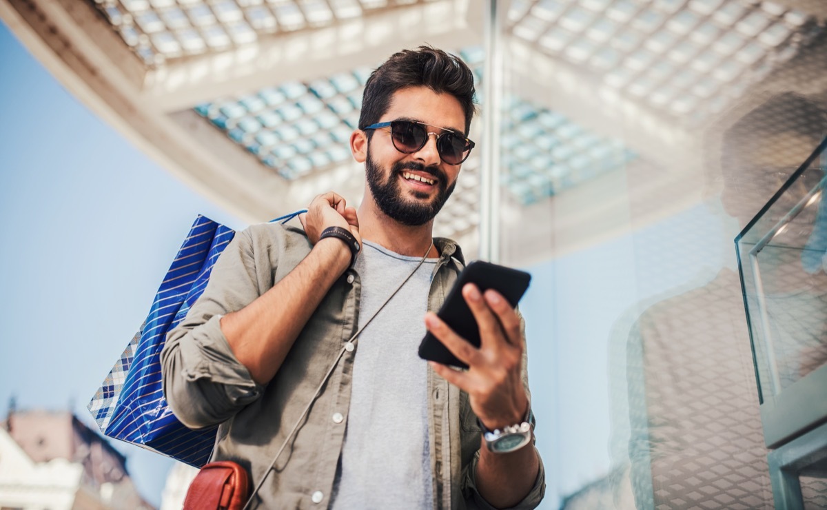 Man with shopping bags smiling at his phone