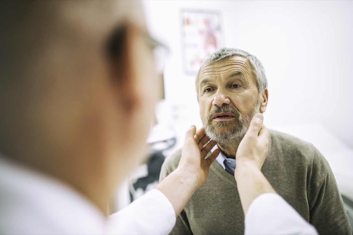 Over the shoulder view of a doctor touching a patient's throat while doing a medical exam.