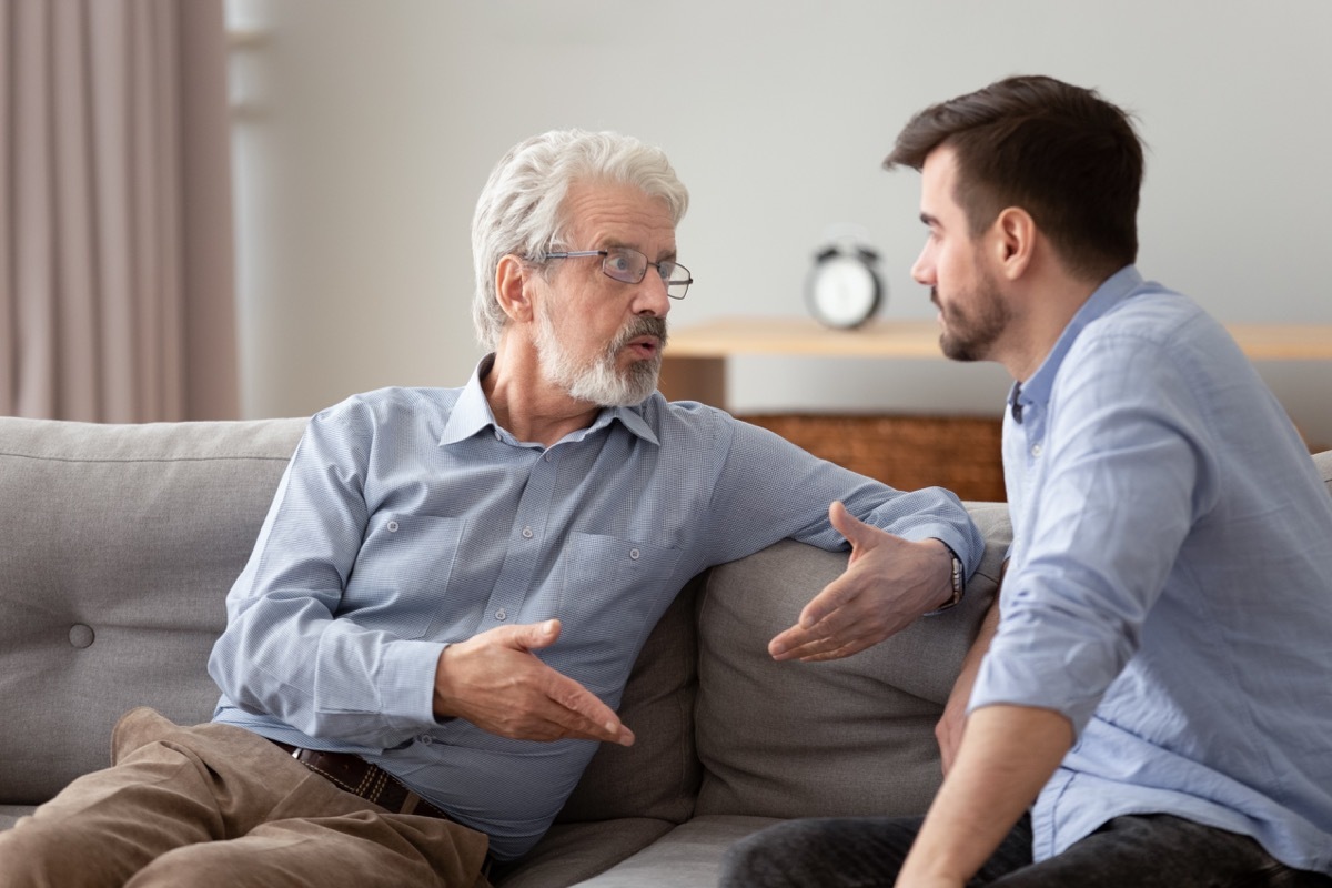 elderly father and grown up adult son sitting on sofa talking