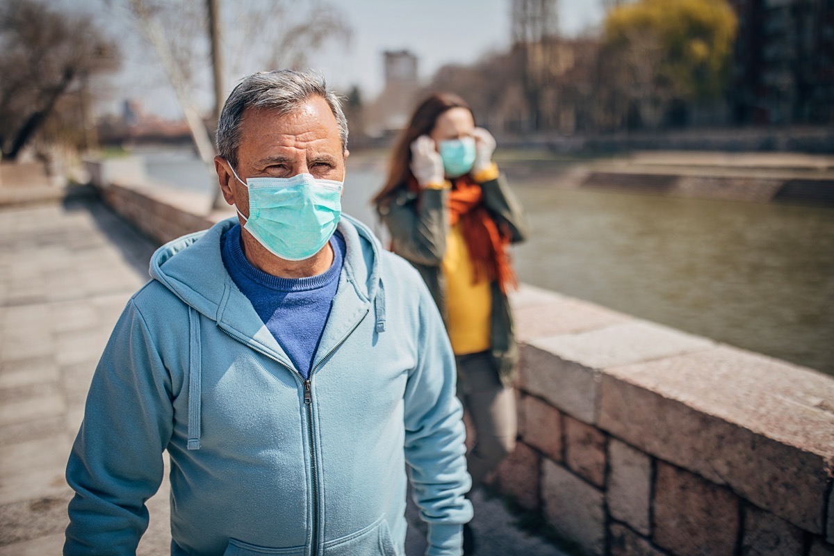 Man and woman, two people with protective mask walking and talking on the street in safe distance.