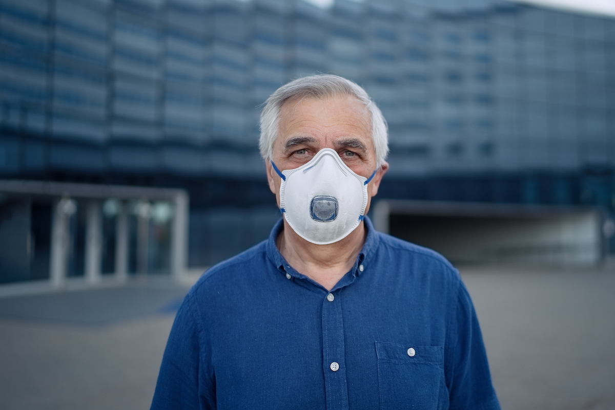senior man wearing mask with respirator in front of office building