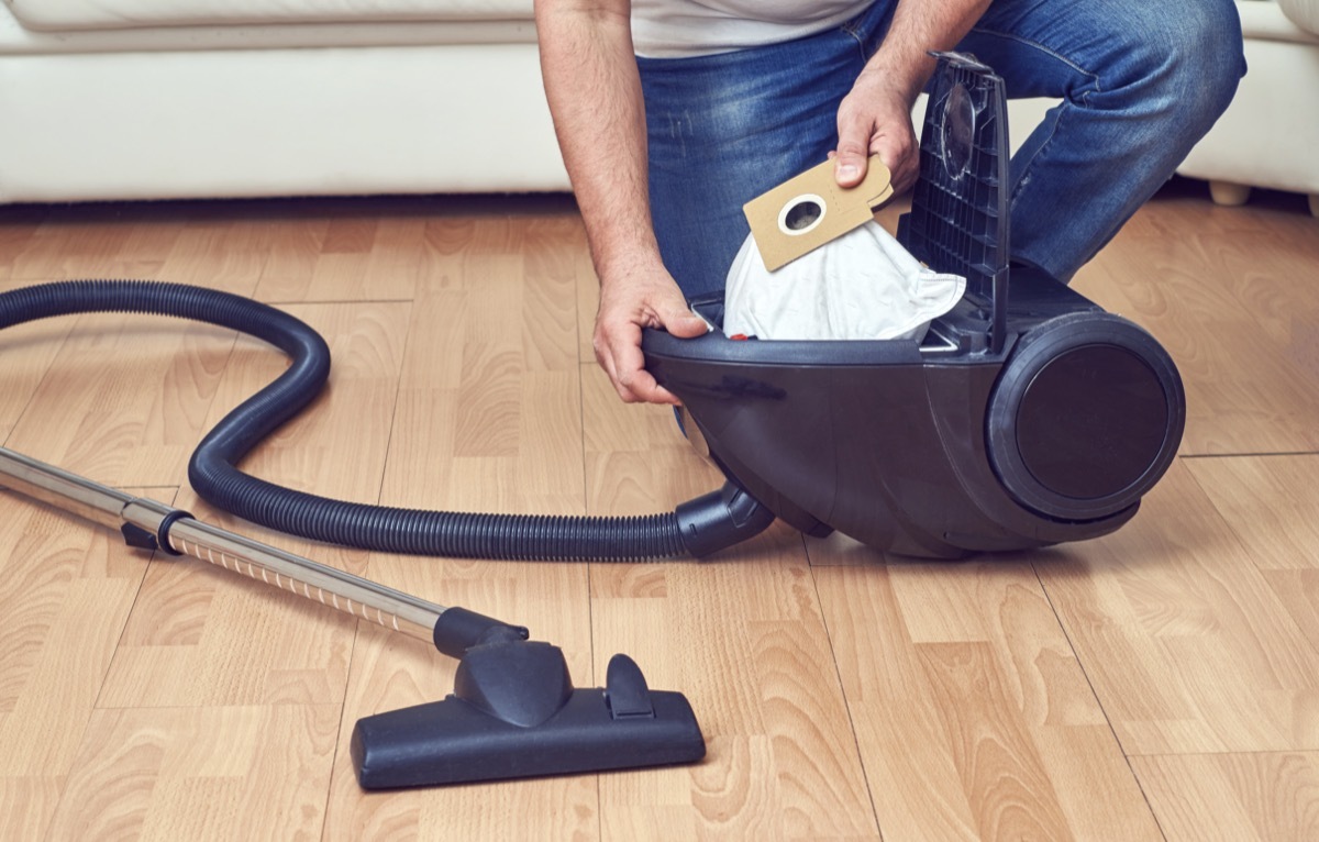 Man taking out a full dust bag from a vacuum cleaner.