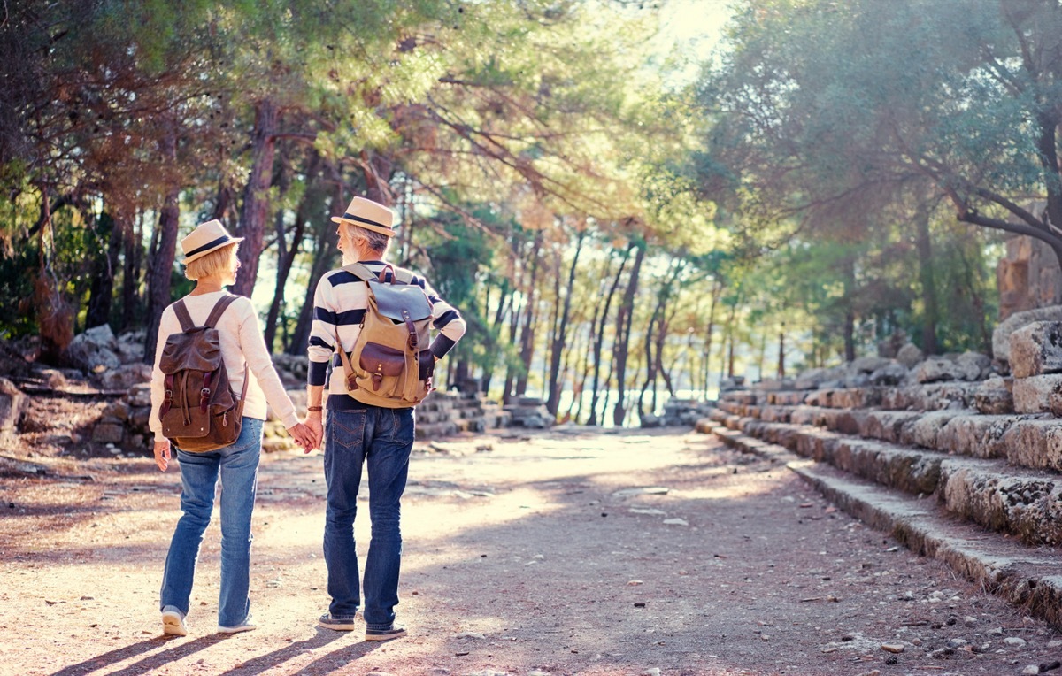 A senior couple walk across a forest.