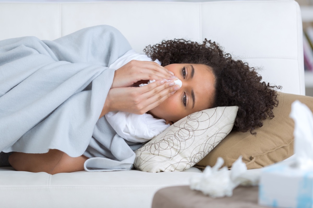 woman on couch sneezing into tissue, signs your cold is serious