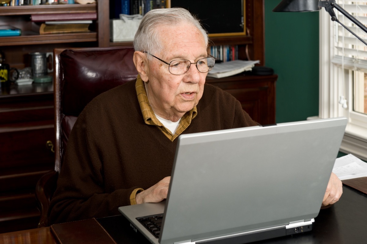 older man looking at laptop in home office