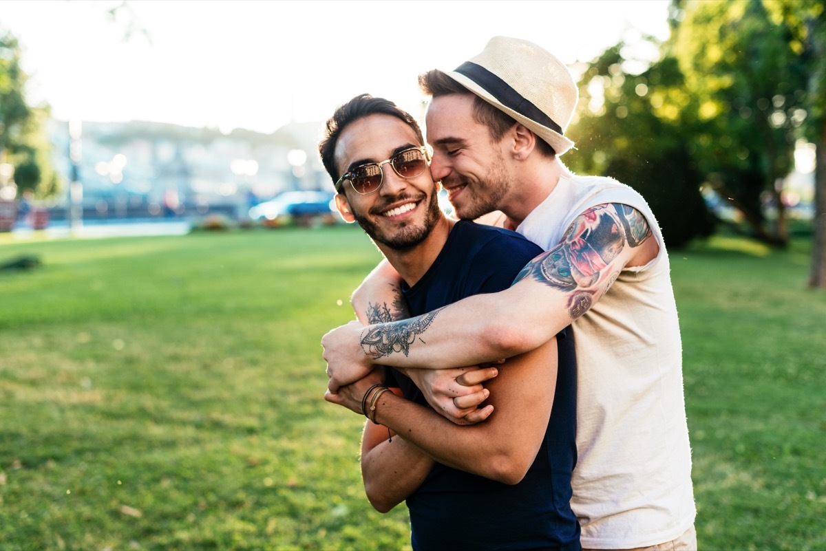 Male couple spending time together hugging on a park date outside