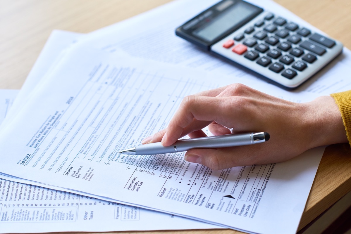 Close-up of unrecognizable woman working with tax return form: she checking papers and using calculator