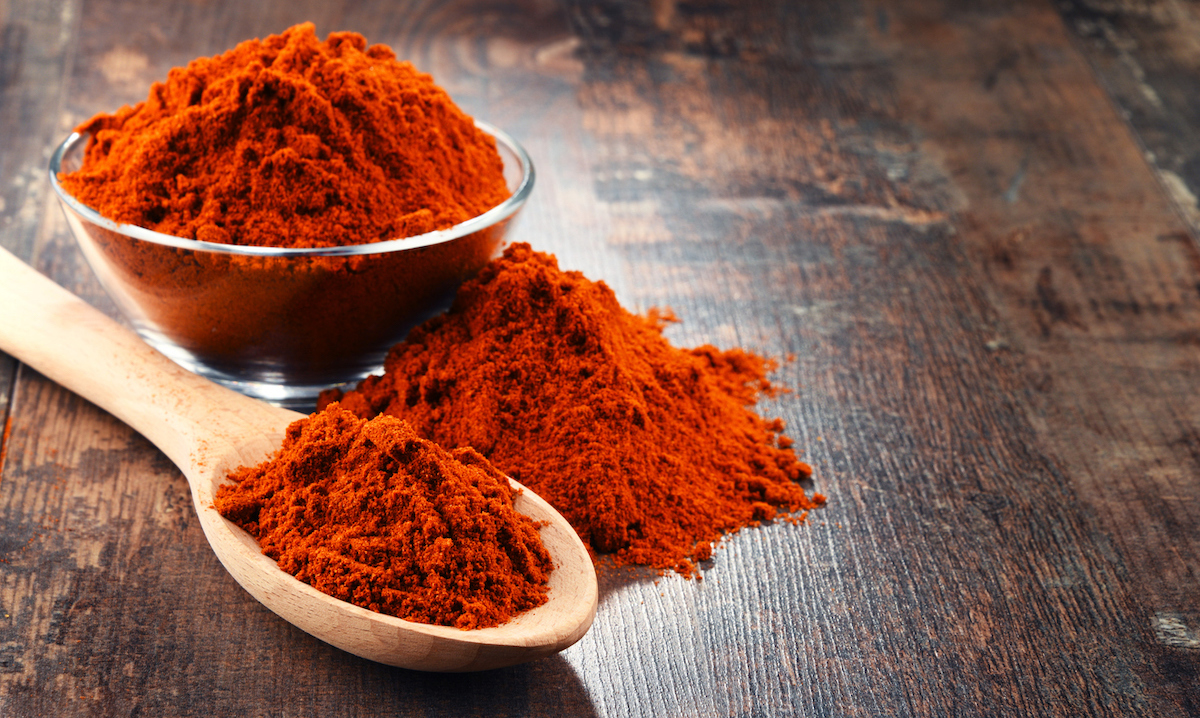 spoon and bowl of cayenne pepper powder on wooden table.
