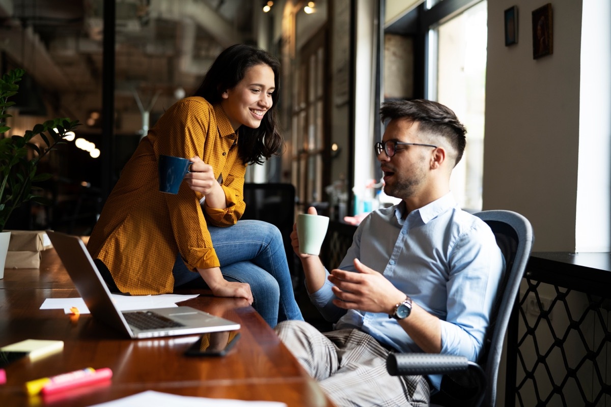 woman sitting on the desk of male coworker