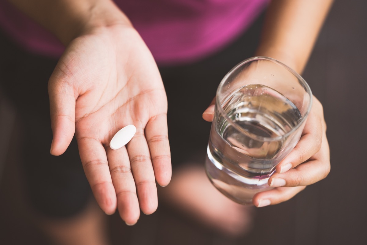 Woman holding hands out with a glass of water in one and a white supplement in the other