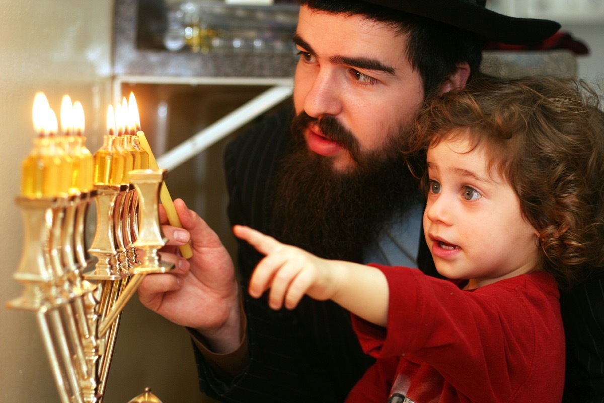young boy with curly hair watching father light menorah