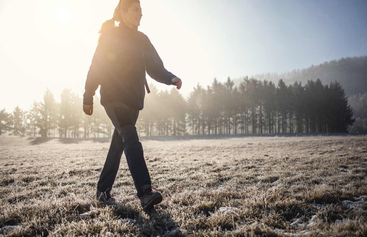 Woman walking across frosted field at dawn
