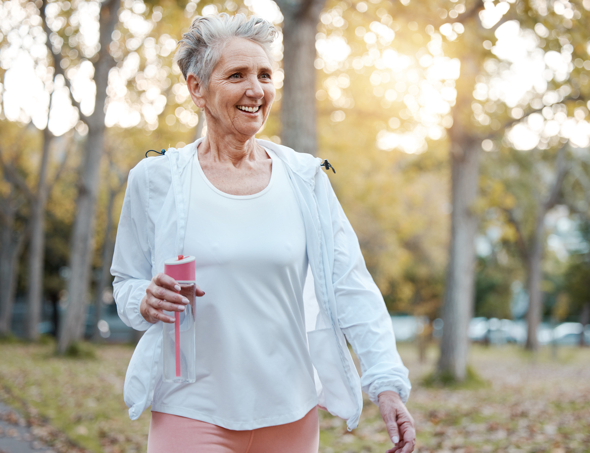 Older woman with short gray hair walking outside holding a water bottle.