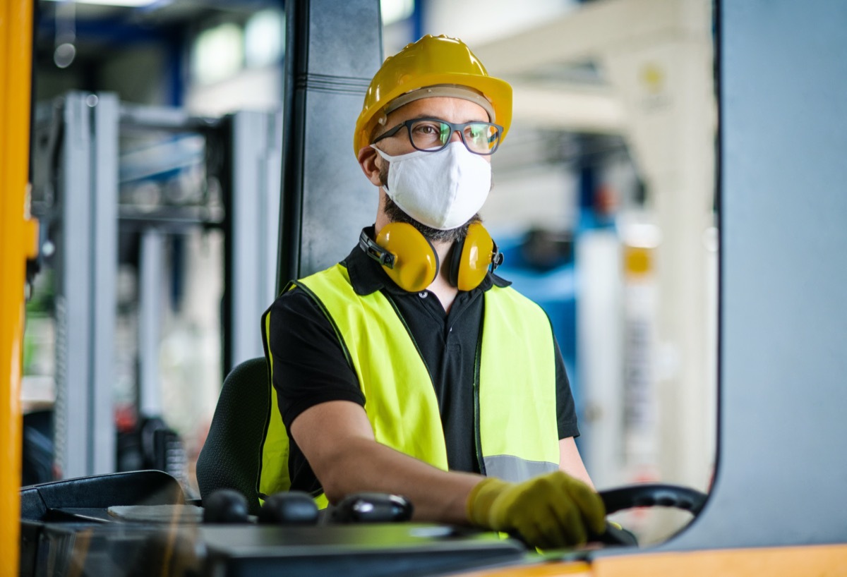 Man worker forklift driver with protective mask working in industrial factory or warehouse.