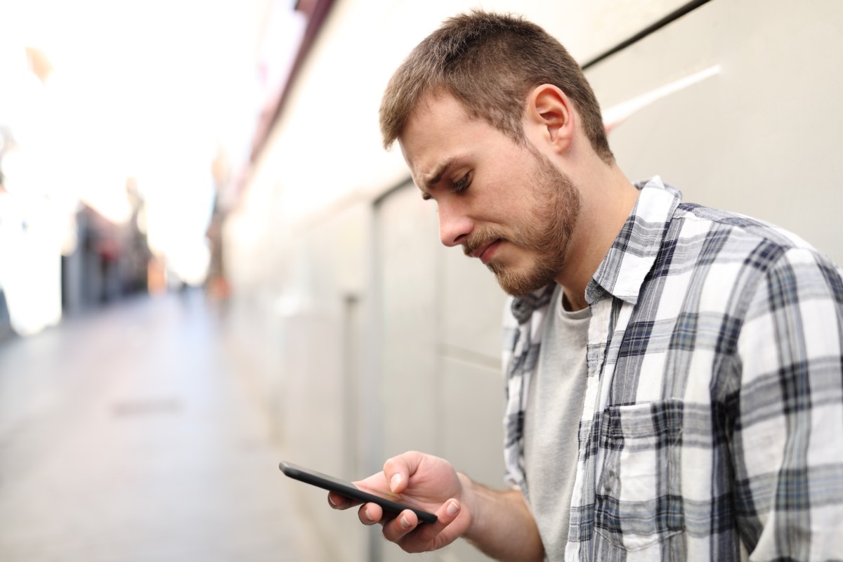 Side view portrait of a sad man in a lonely street using a smart phone