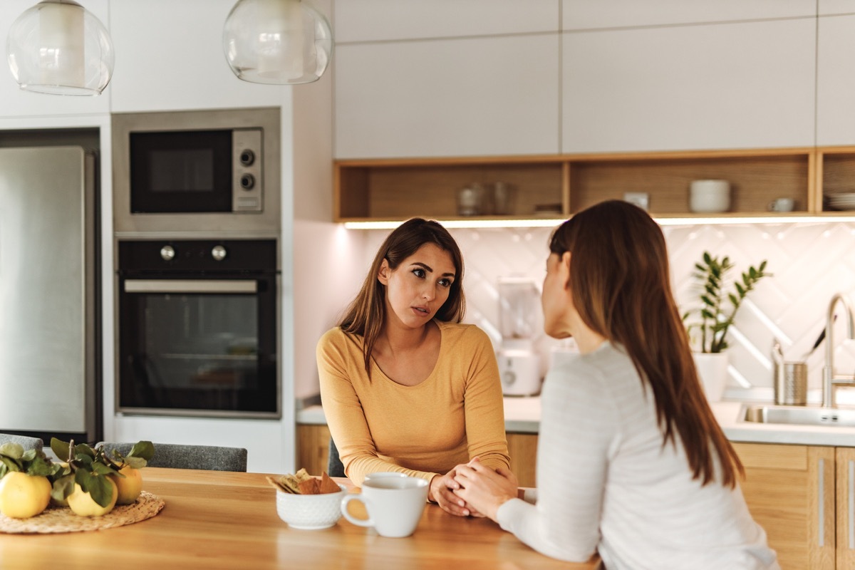 two woman talking at a kitchen counter, holding hands across the surface