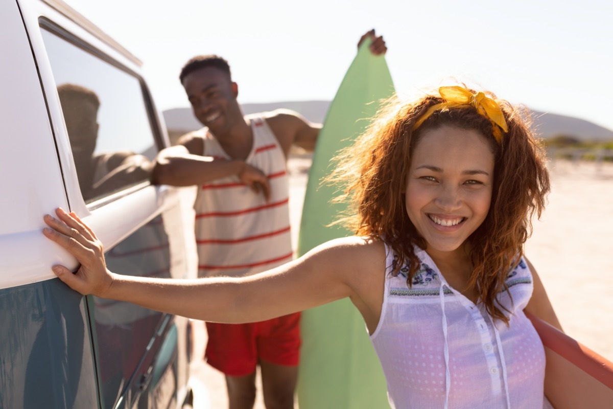 young couple holding surfboards outside van