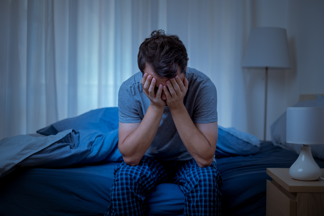 Man sitting on his bed with his head in his hands.