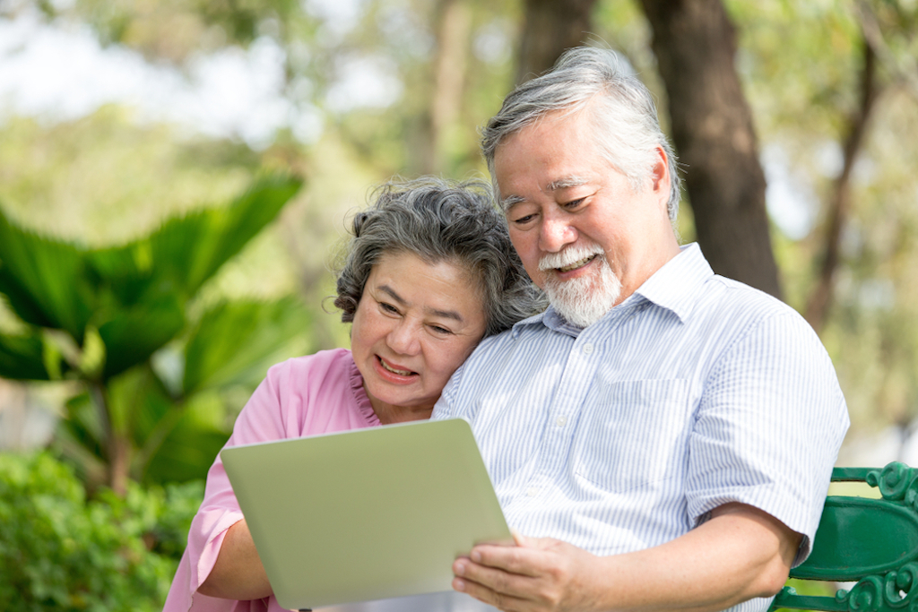 older couple sitting outside on a bench using a tablet