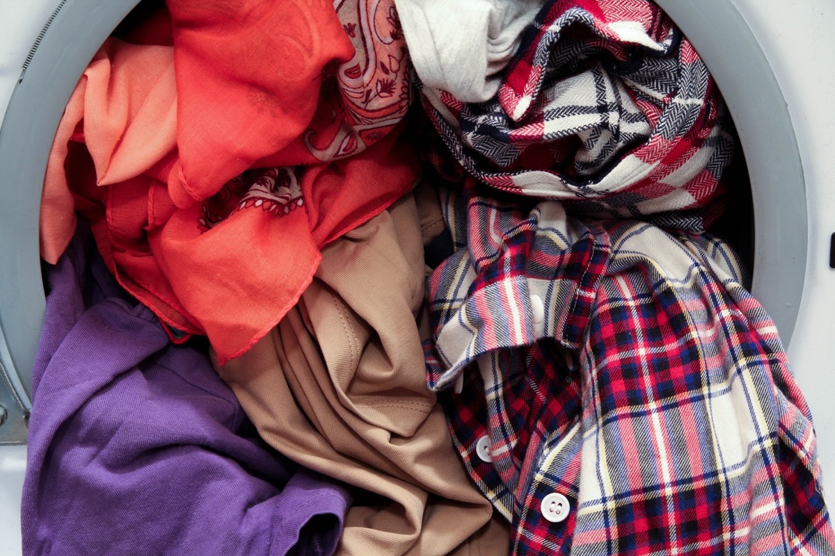 Front loading washing machine overloaded with colorful dirty clothes, close up view - Image