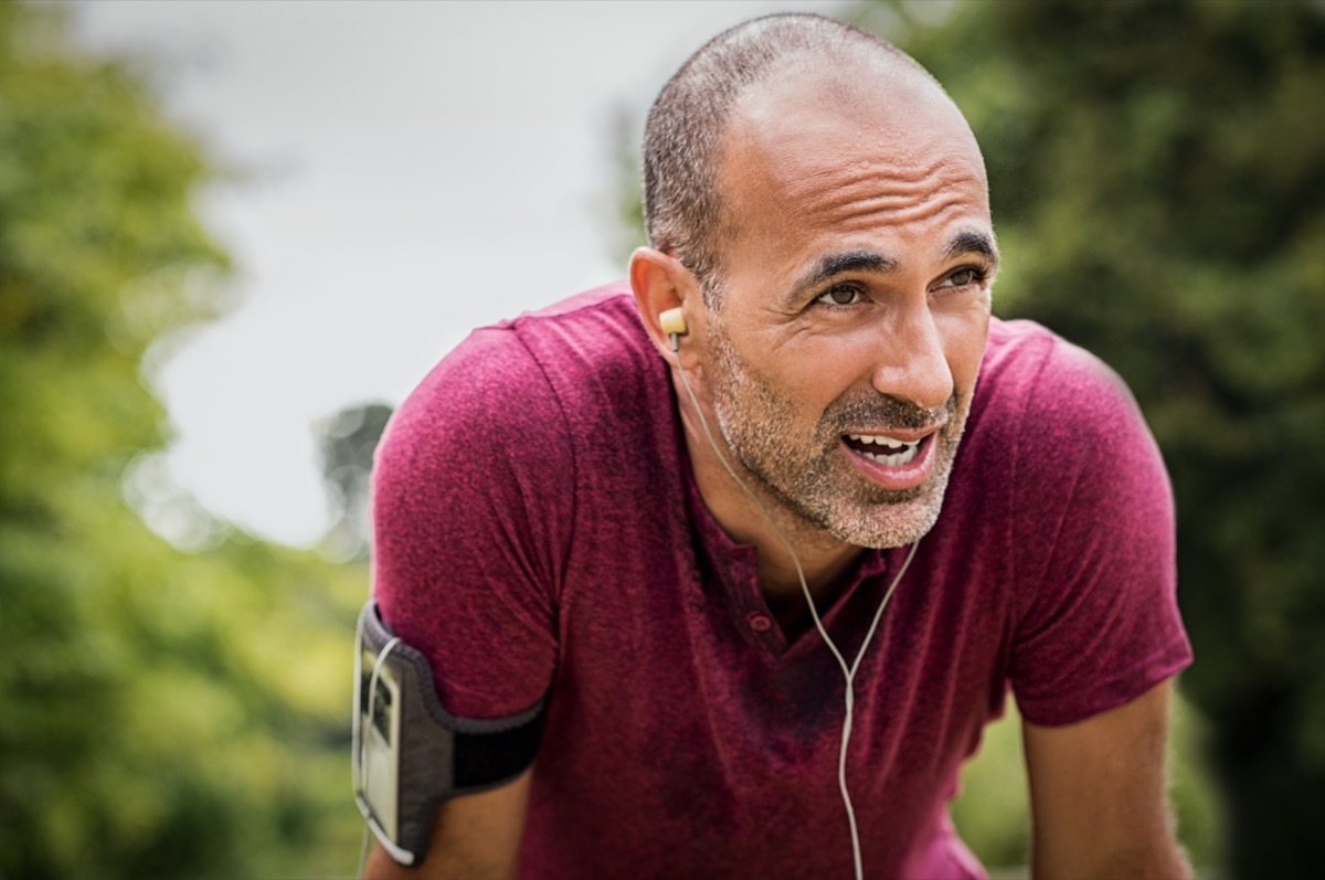mature man after run. Handsome senior man resting after jog at the park on a sunny day. Sweaty multiethnic man listening to music while jogging