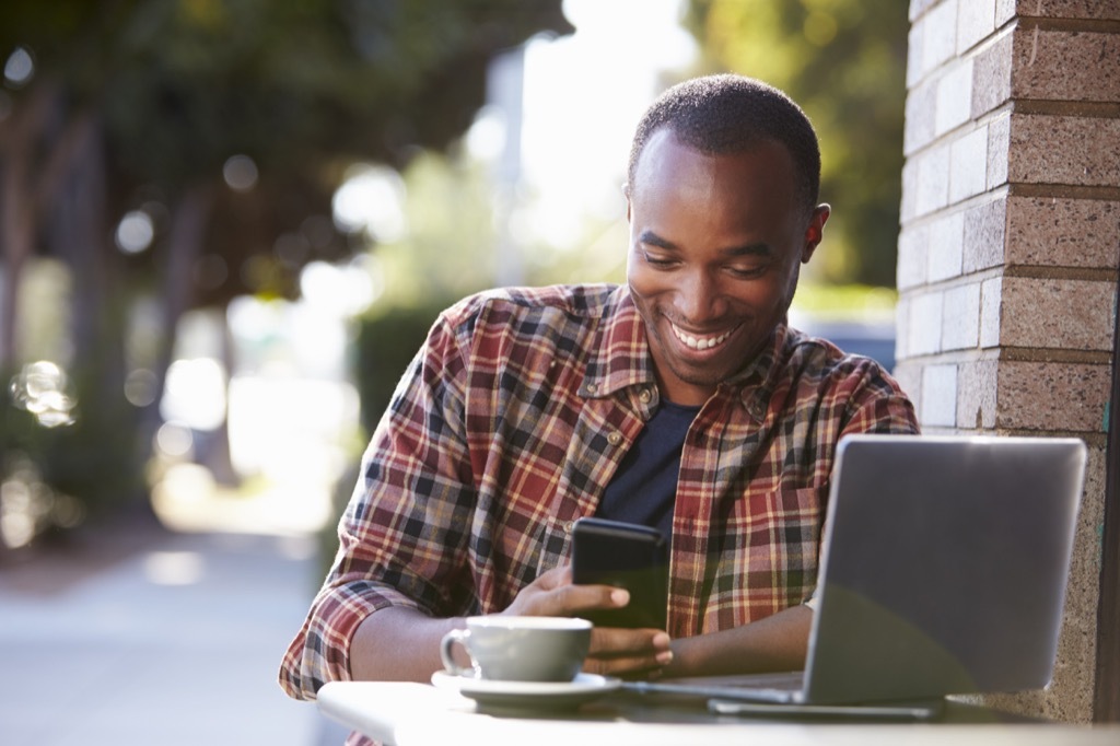 Man sitting outside at coffeeshop using phone and laptop