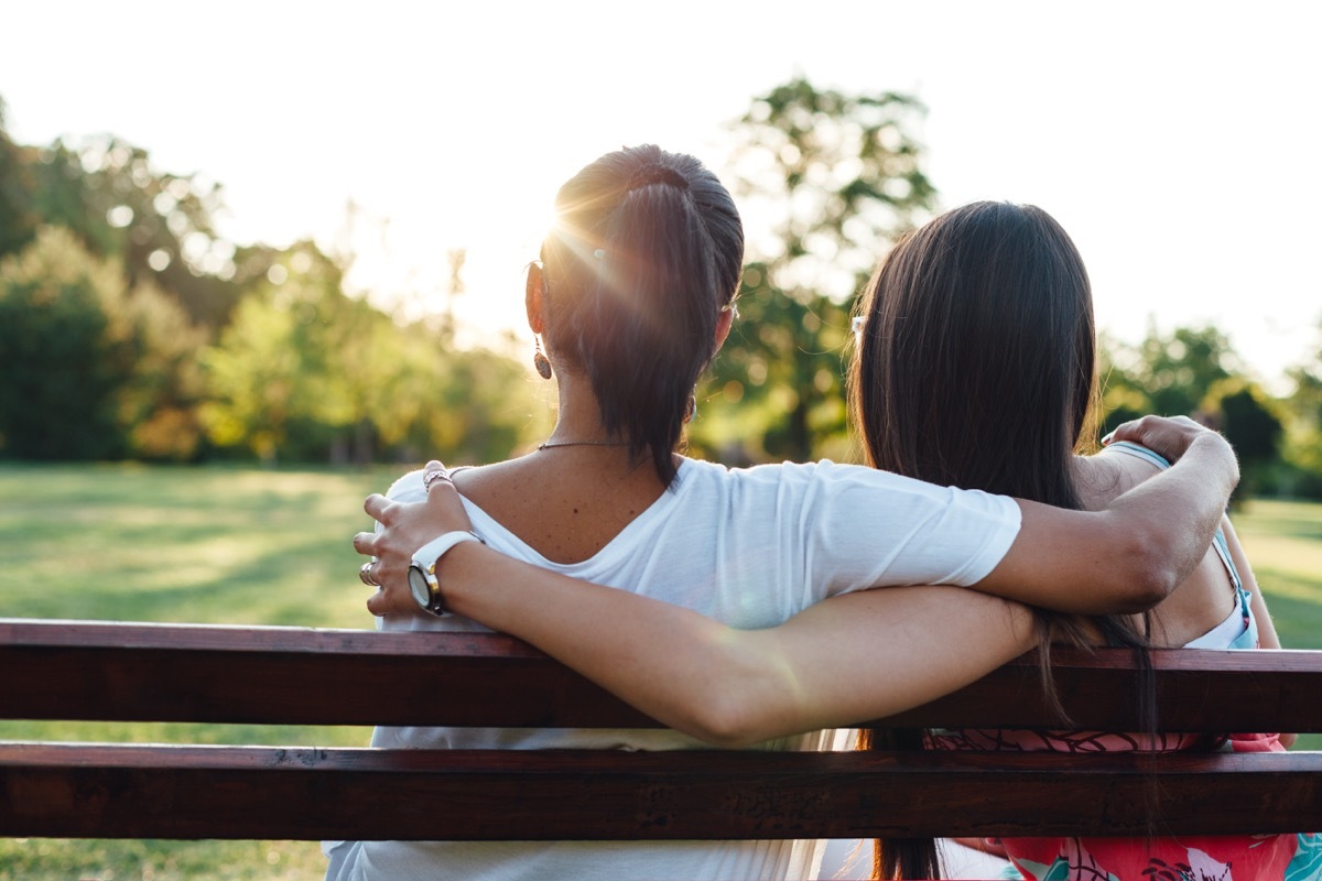 Mom and daughter sit on park bench looking at sunset, what it's like being a teen mom