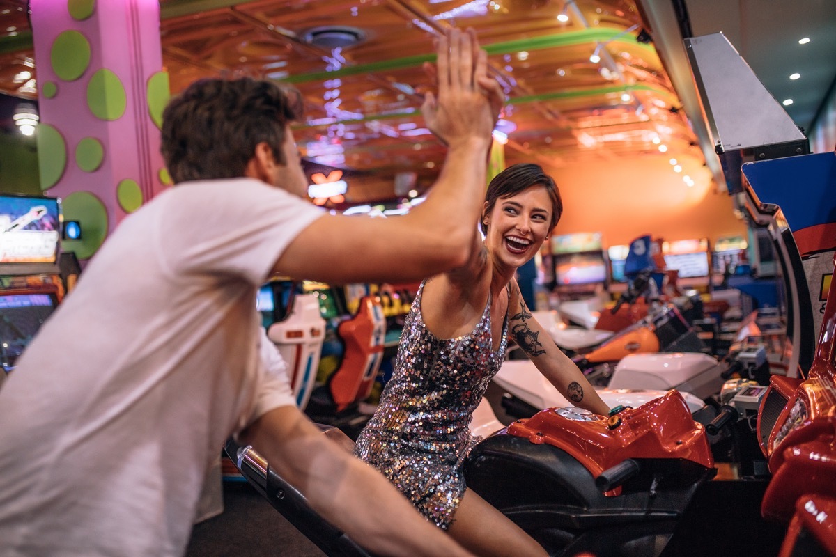 Couple giving high five to each other while playing bike racing games at a gaming arcade. Couple enjoying arcade racing games at a gaming parlour