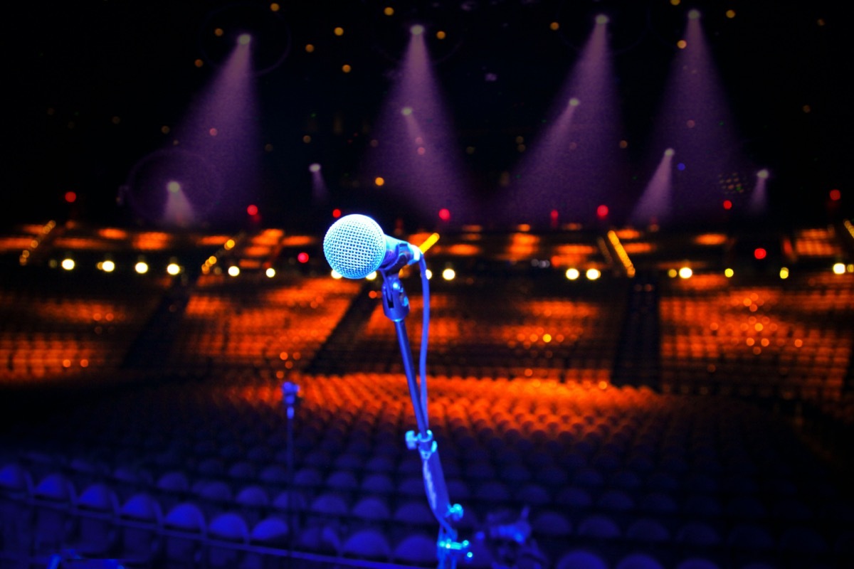 Microphone on stage overlooking a large empty concert venue - show cancellation or stage fright concept