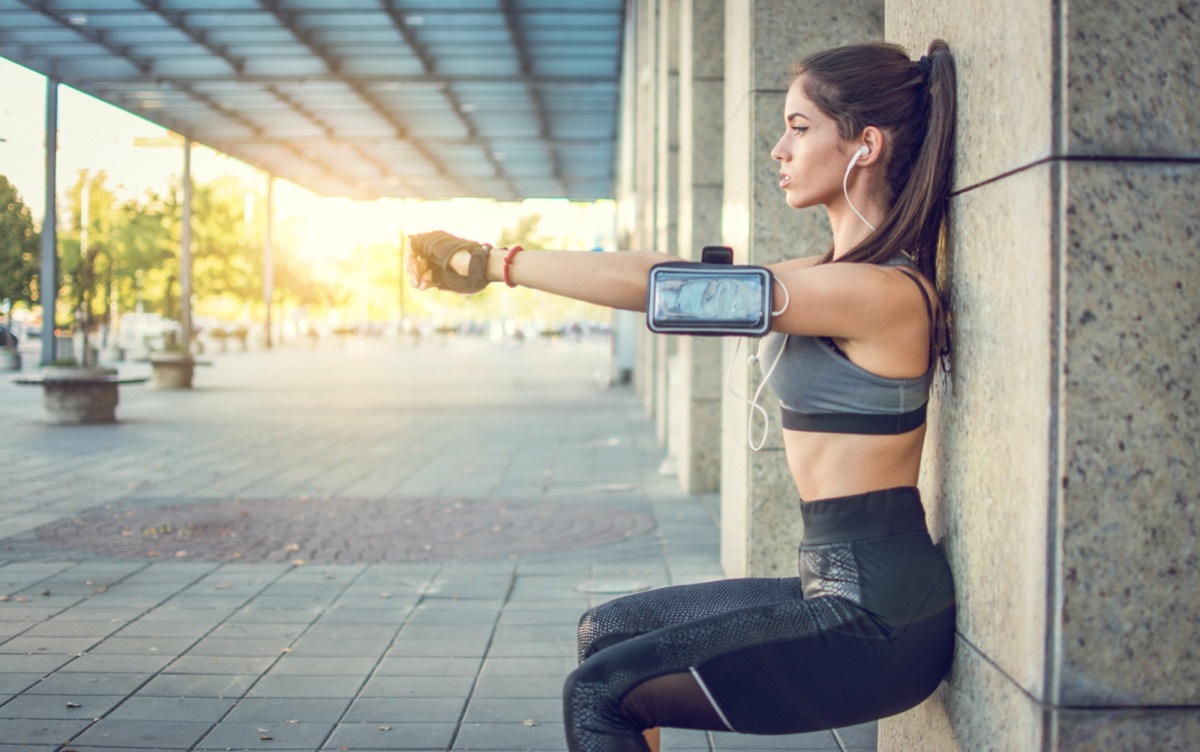Young athletic woman doing squats against wall outdoors.