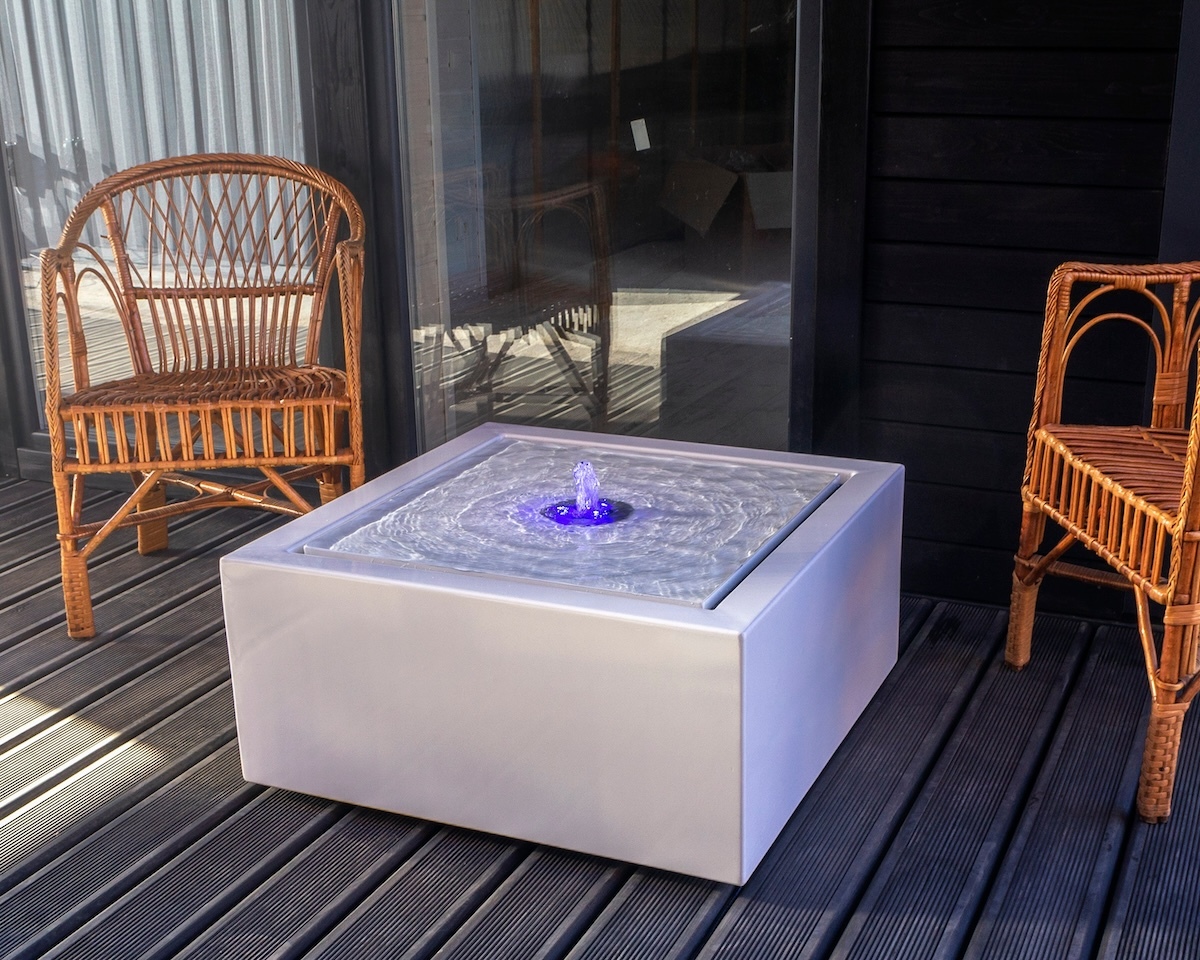 white, square water table on a deck with two rattan chairs next to it