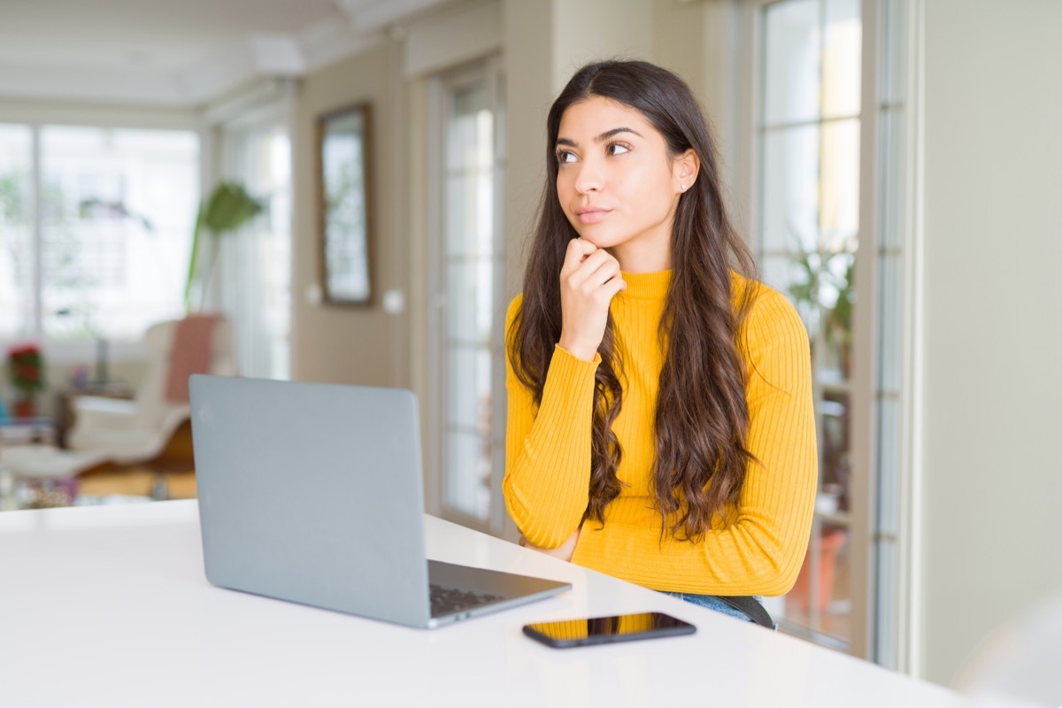 Young woman using computer laptop with hand on chin thinking about question, pensive expression. Smiling with thoughtful face. Doubt concept.