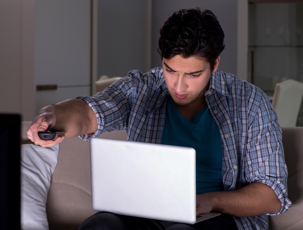 young man video chatting on laptop while watching tv