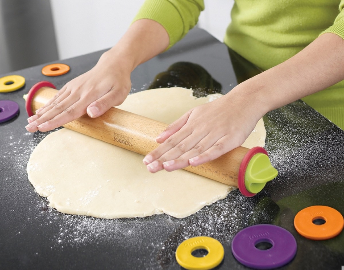 white hands rolling out dough with wooden rolling pin