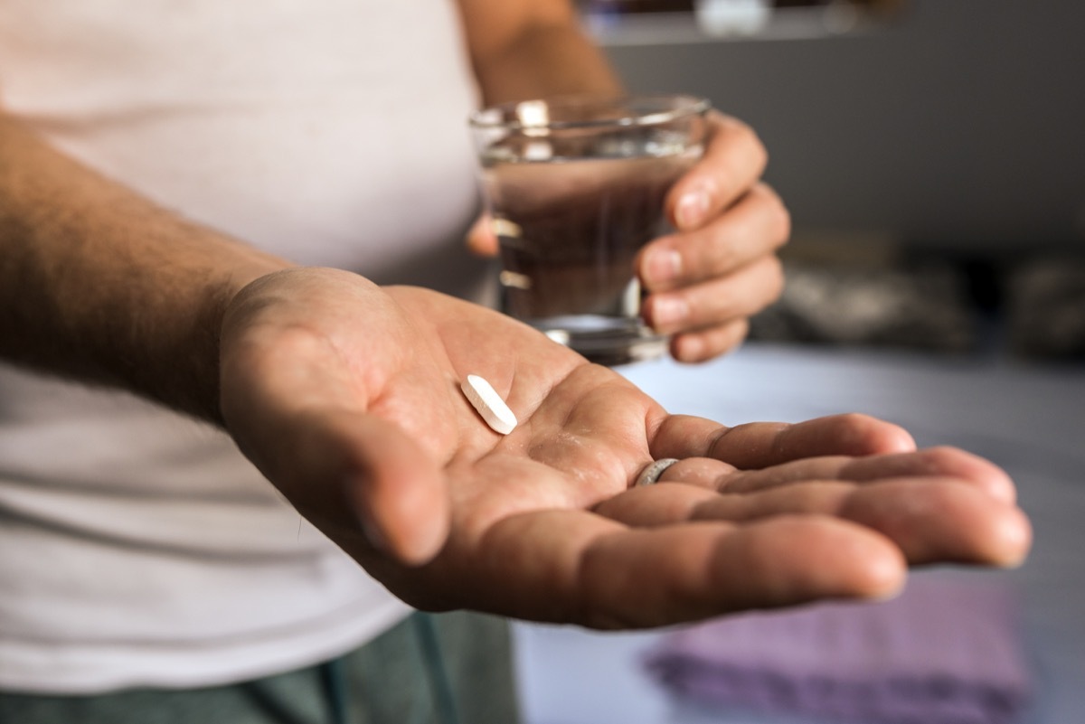 age, medicine, healthcare and people concept - close up of mature man hands with white pill and water glass at home. Health care and medical concept. Male taking medication, feeling ill. he is going to take some medicine