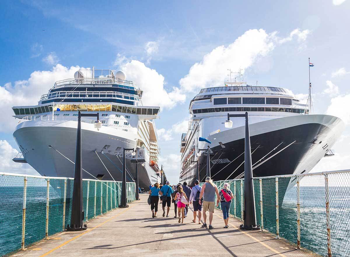 a crowd of people walk toward two cruise ships at port