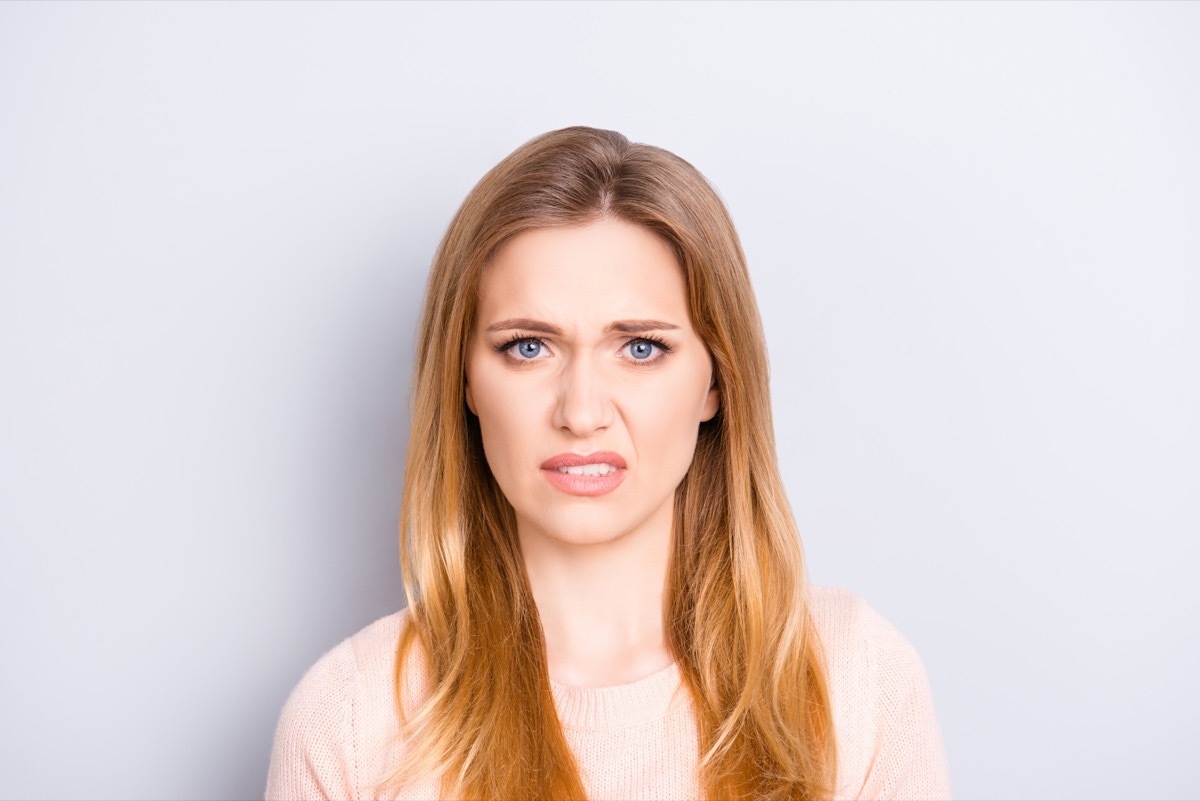 Close up portrait of funny confused puzzled unhappy upset sad uncertain unsure beautiful pretty charming grimacing woman with long blonde hairdo isolated on gray background opy-space