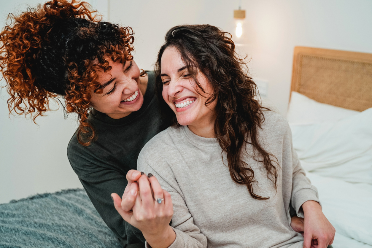 Two women laughing and embracing in bed