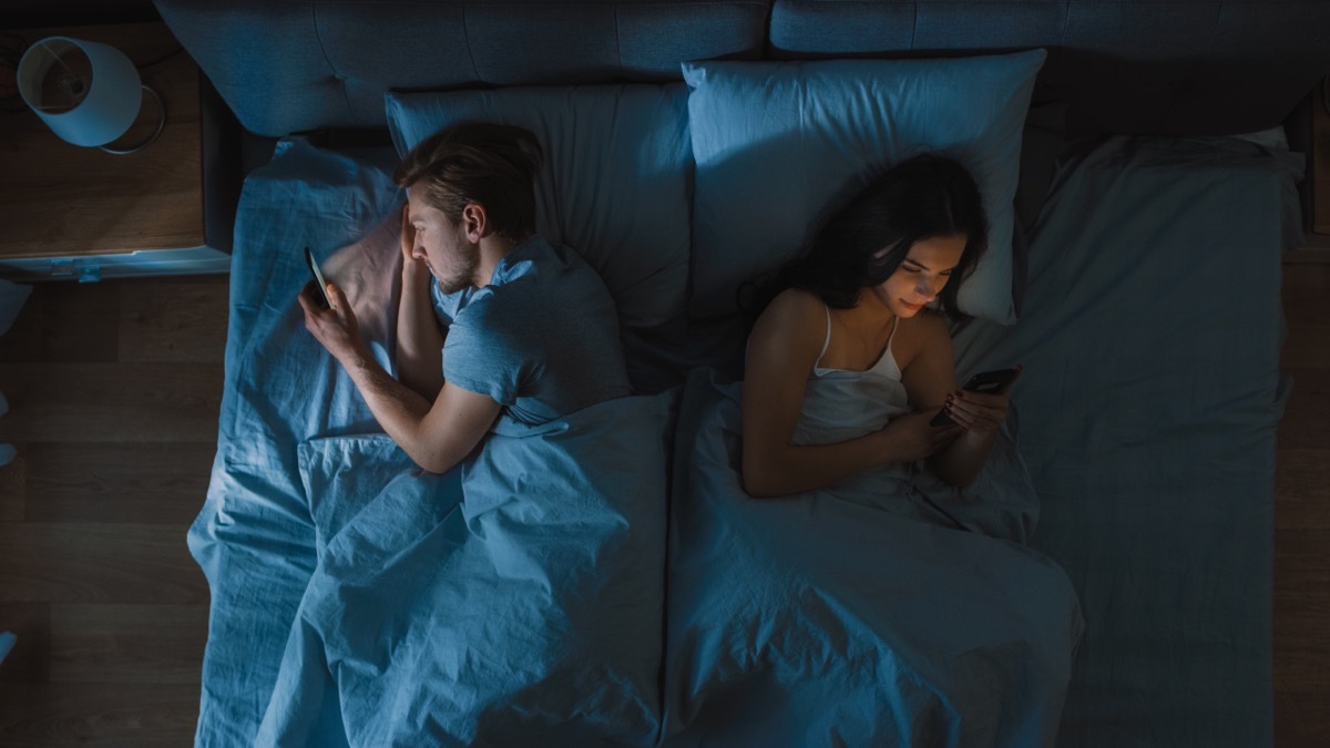 Couple sleeping in the same bed on their phones.