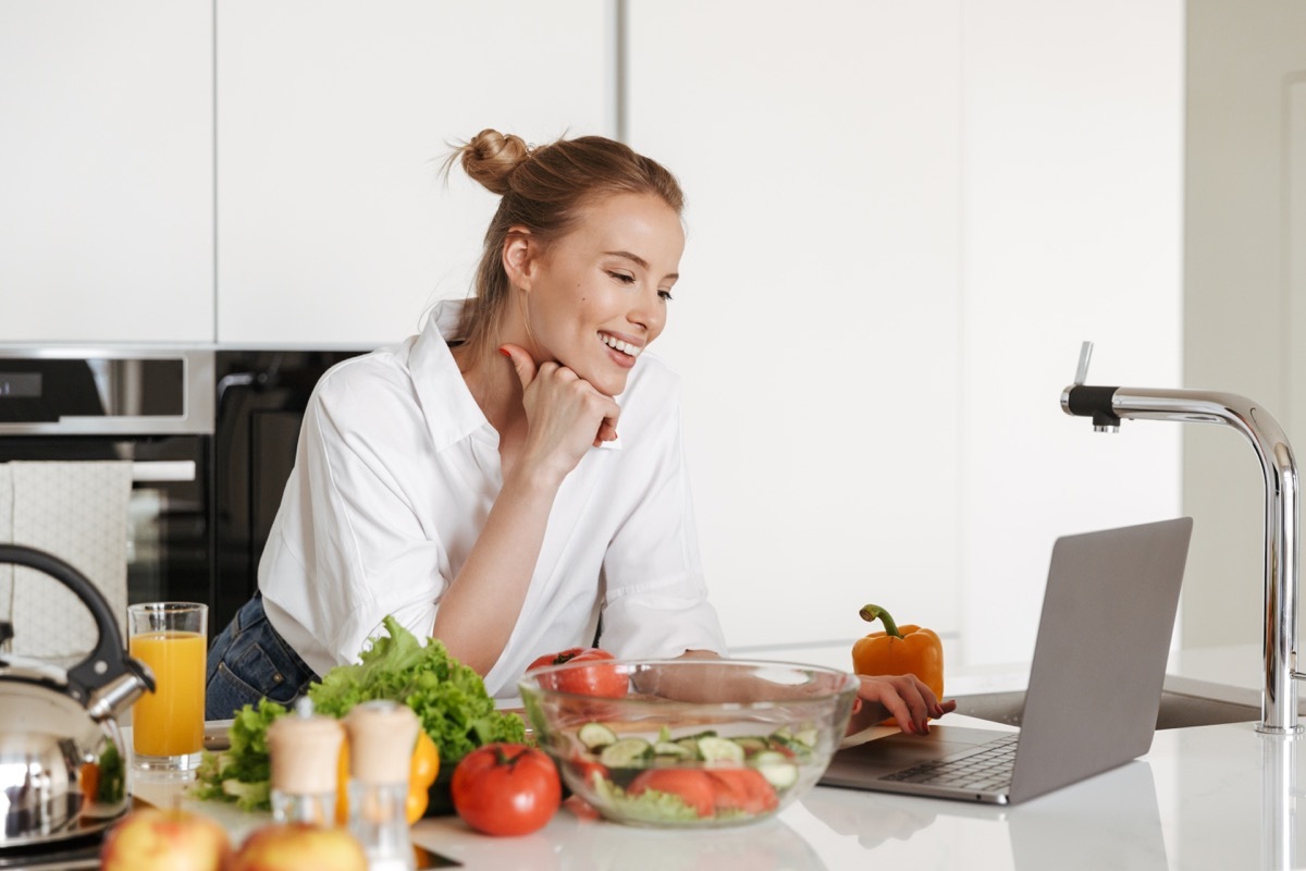 Woman cooking in kitchen with her laptop