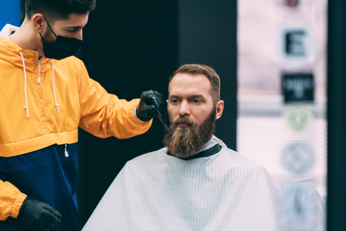 Barber with face mask combing customer