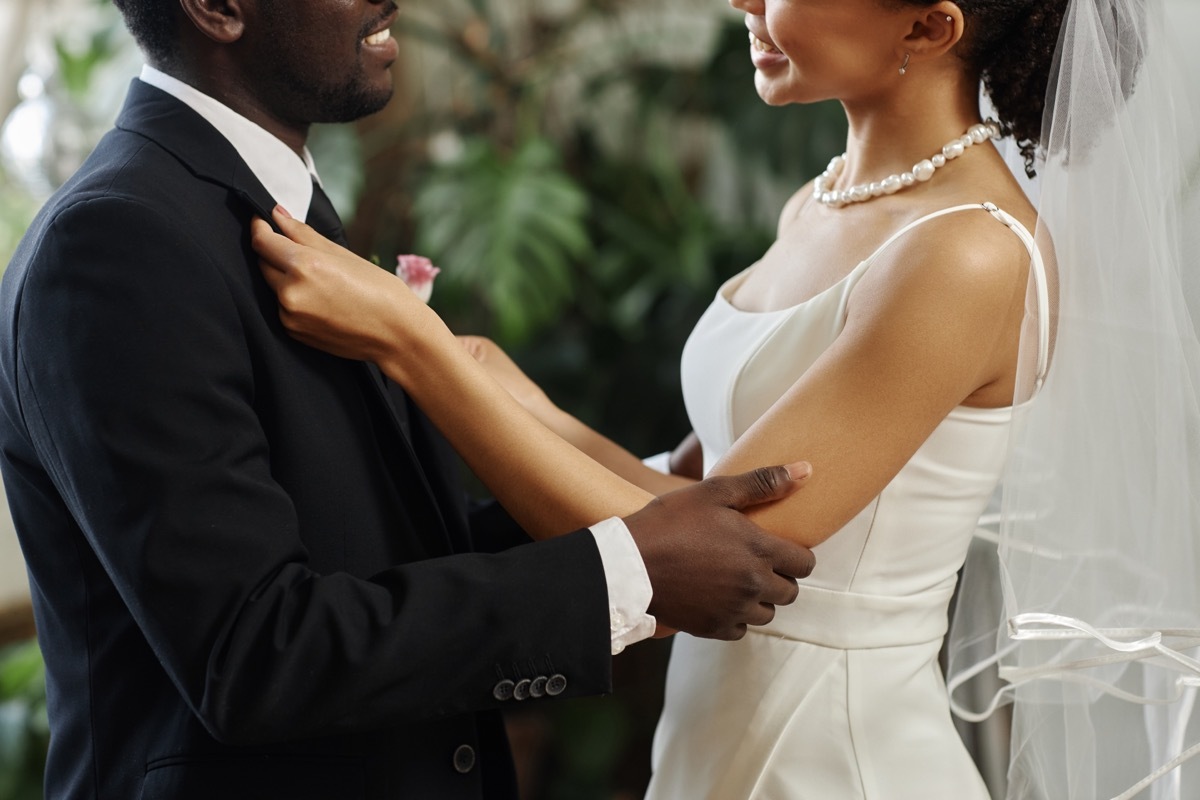 Side view closeup of young couple getting married with bride adjusting jacket and boutonniere before wedding ceremony