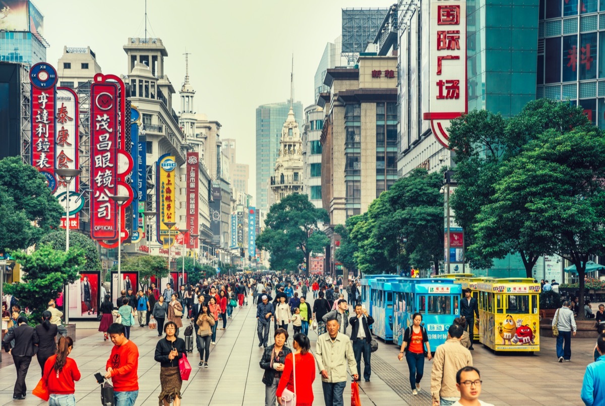 Crowds walk below neon signs on Nanjing Road. The street is the main shopping district of the city and one of the world's busiest shopping districts.
