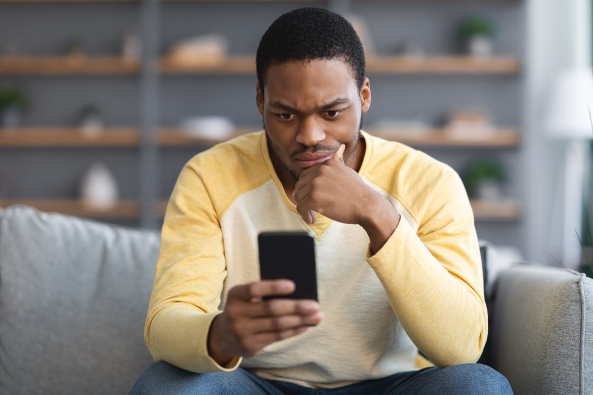 man looking suspiciously at his phone while sitting on the couch