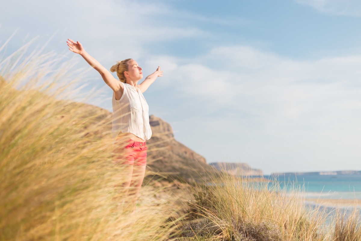 Relaxed woman, arms rised, enjoying sun, freedom and life an a beautiful beach. Young lady feeling free, relaxed and happy. Concept of vacations, freedom, happiness, enjoyment and well being.