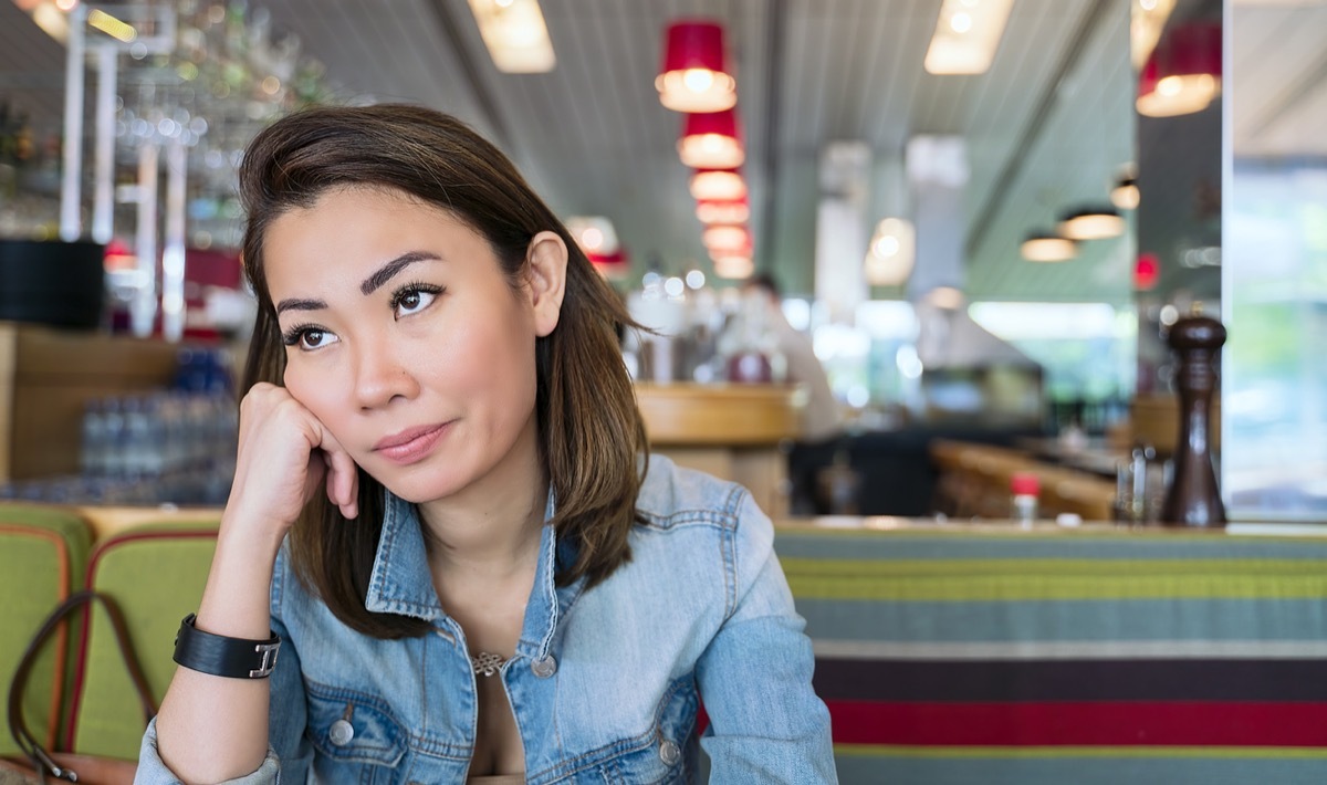 young woman looking annoyed and rolling her eyes while sitting in a booth at a diner