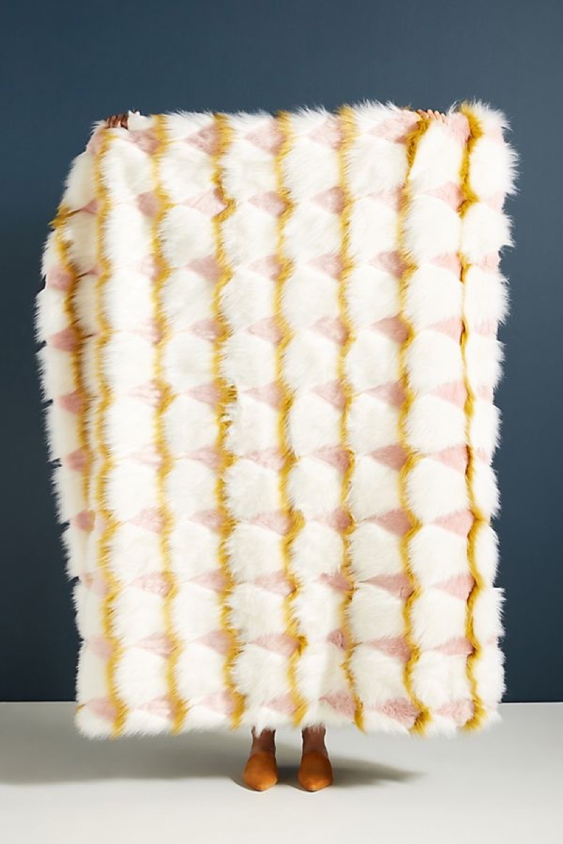 Woman holding white, yellow, prink faux fur throw