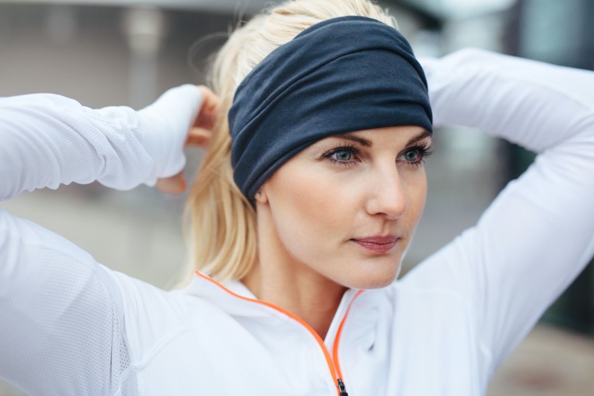 Close-up of young female athlete tying up hair before a run. Sporty fitness woman on outdoor workout looking motivated.
