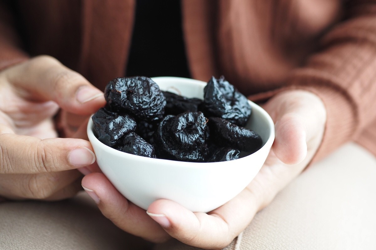 closeup of a woman holding a small bowl of prunes