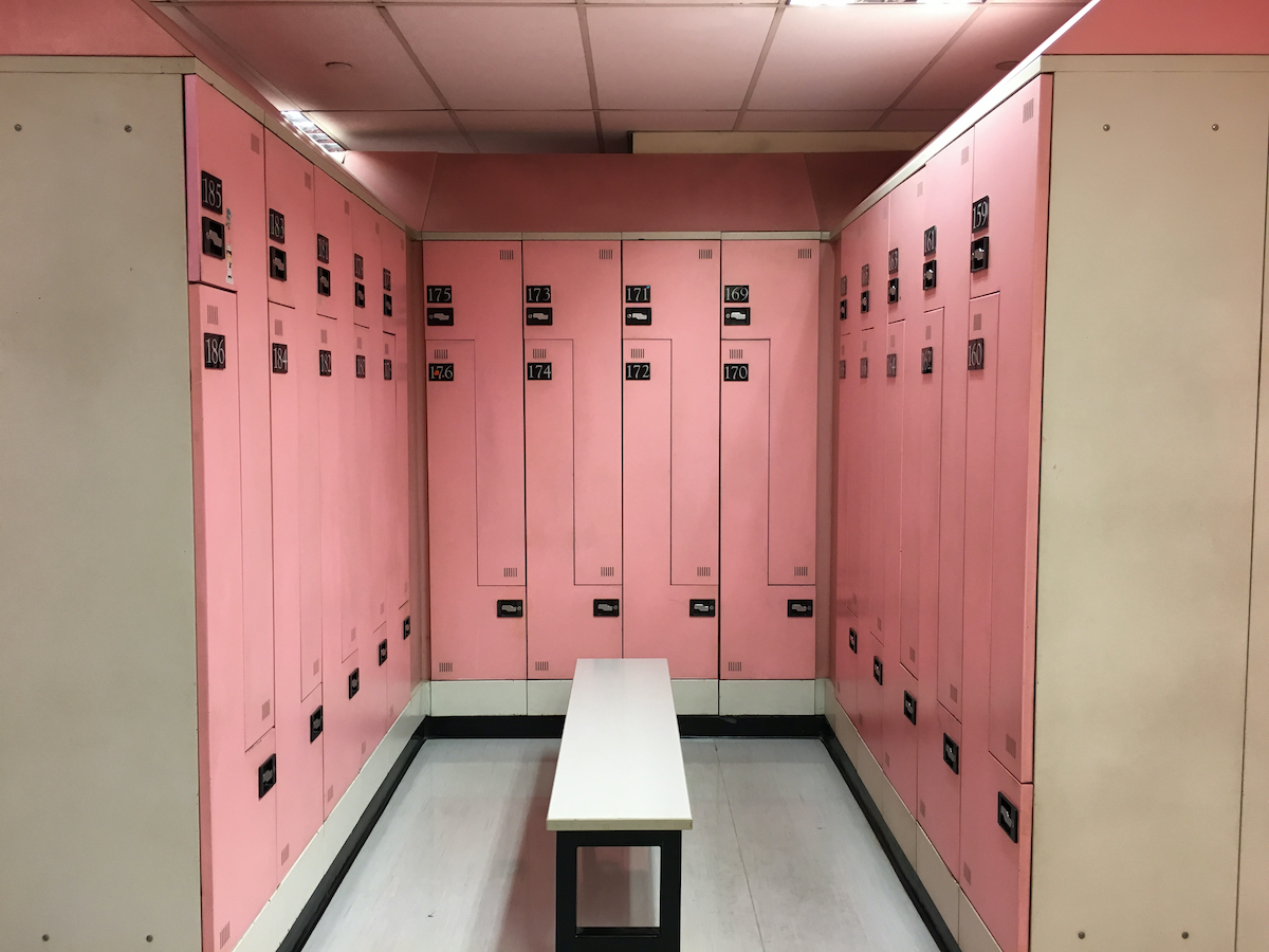 An empty changing room, locker room, dressing room with pink color for female only and there’s a white bench at the center.